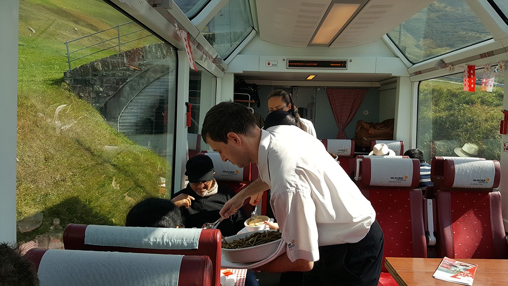 Uitserveren van de lunch in een 1e klas panoramawagon van de Glacier Express trein op de route Zermatt-St. Moritz.