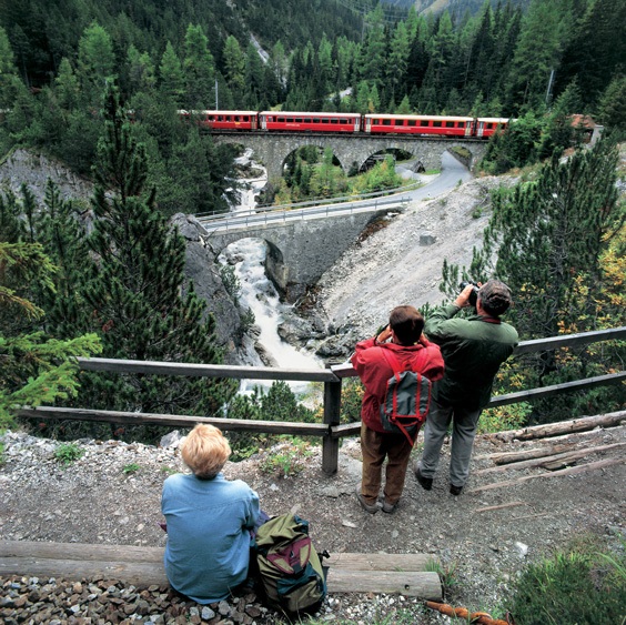 Wandelaars fotograferen de trein van de Rhatische bahn op het traject van de Bernina Express tussen Berguen en Preda.